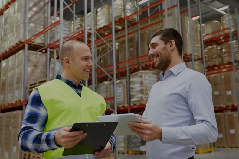 Two people checking stock against a clipboard on a warehouse floor
